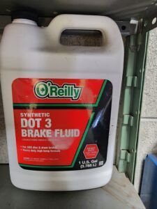 O'Reilly DOT 3 synthetic brake fluid container. White jug with red, green, and black label, 1-gallon size, on a shelf.