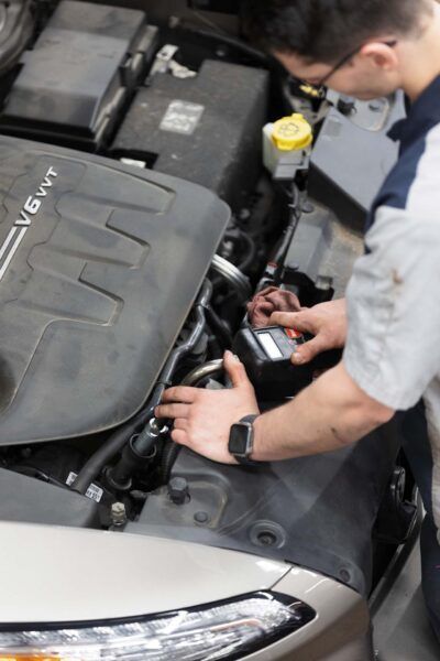 Mechanic working on a car engine under the hood. Holding a tool and examining components.