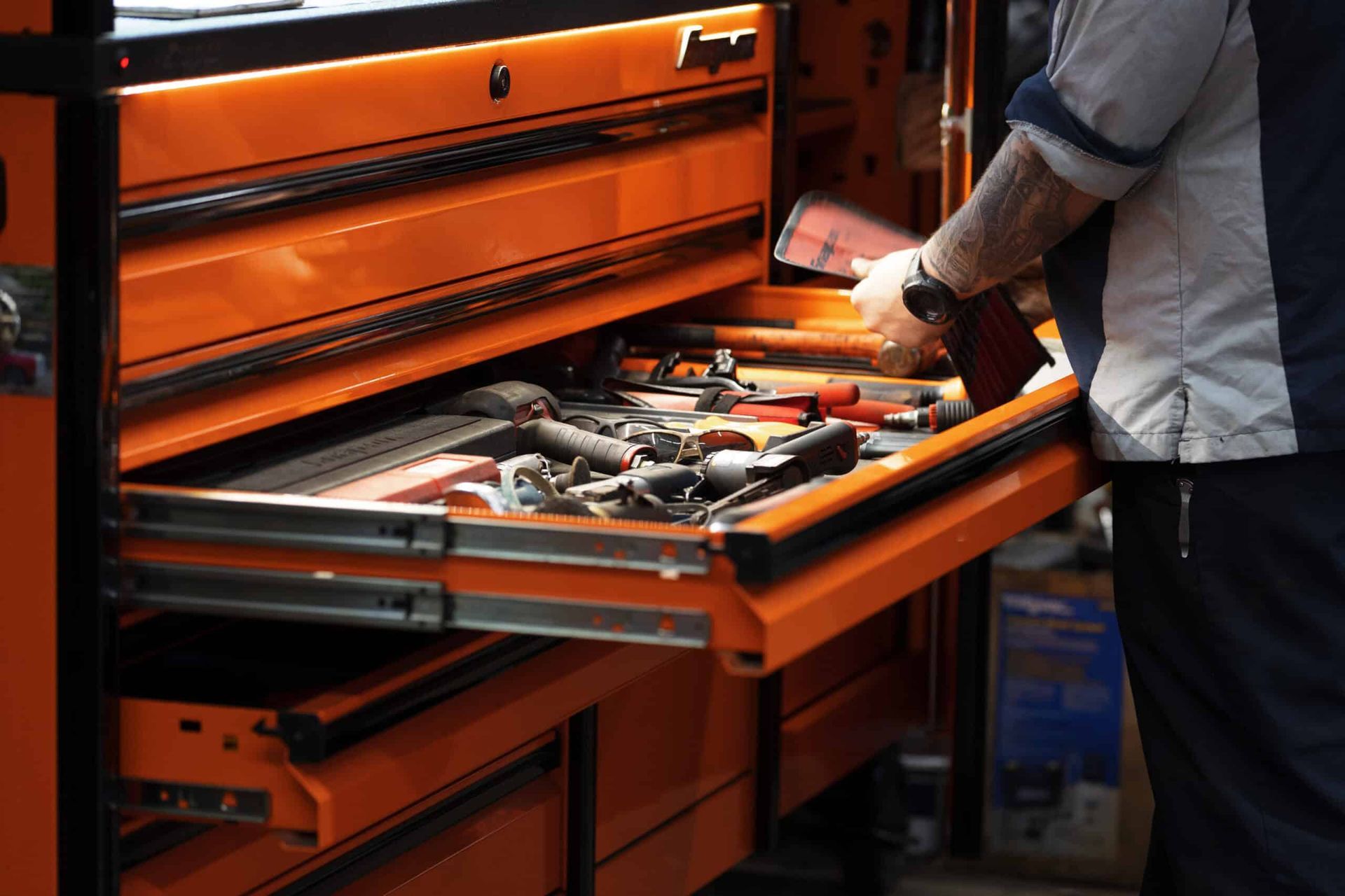 Person reaching into an open orange toolbox drawer filled with tools.
