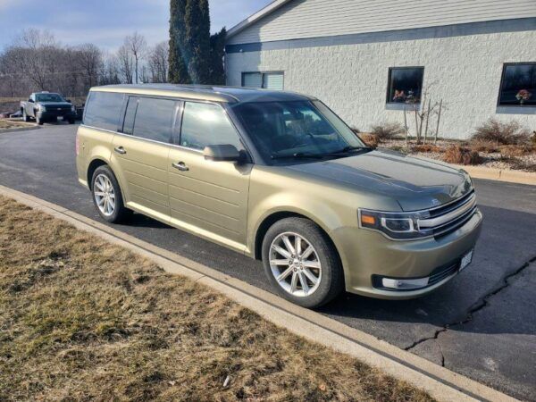Gold Ford Flex parked on a paved road next to a building on a sunny day.