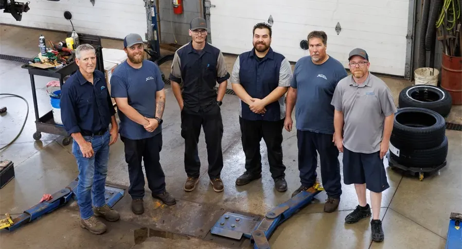 Six technicians stand together indoors; smiling, inside our garage | Joe's Slinger Service, LLC