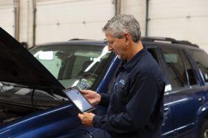 Mechanic using a tablet to diagnose a blue car's engine in a garage.