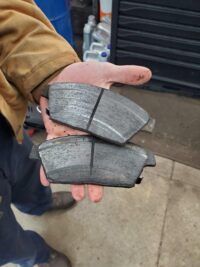 Hand holding two worn brake pads.