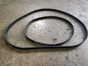 A black serpentine belt coiled on a concrete surface.