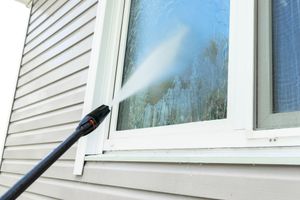 Pressure washer spraying a house window and siding with water