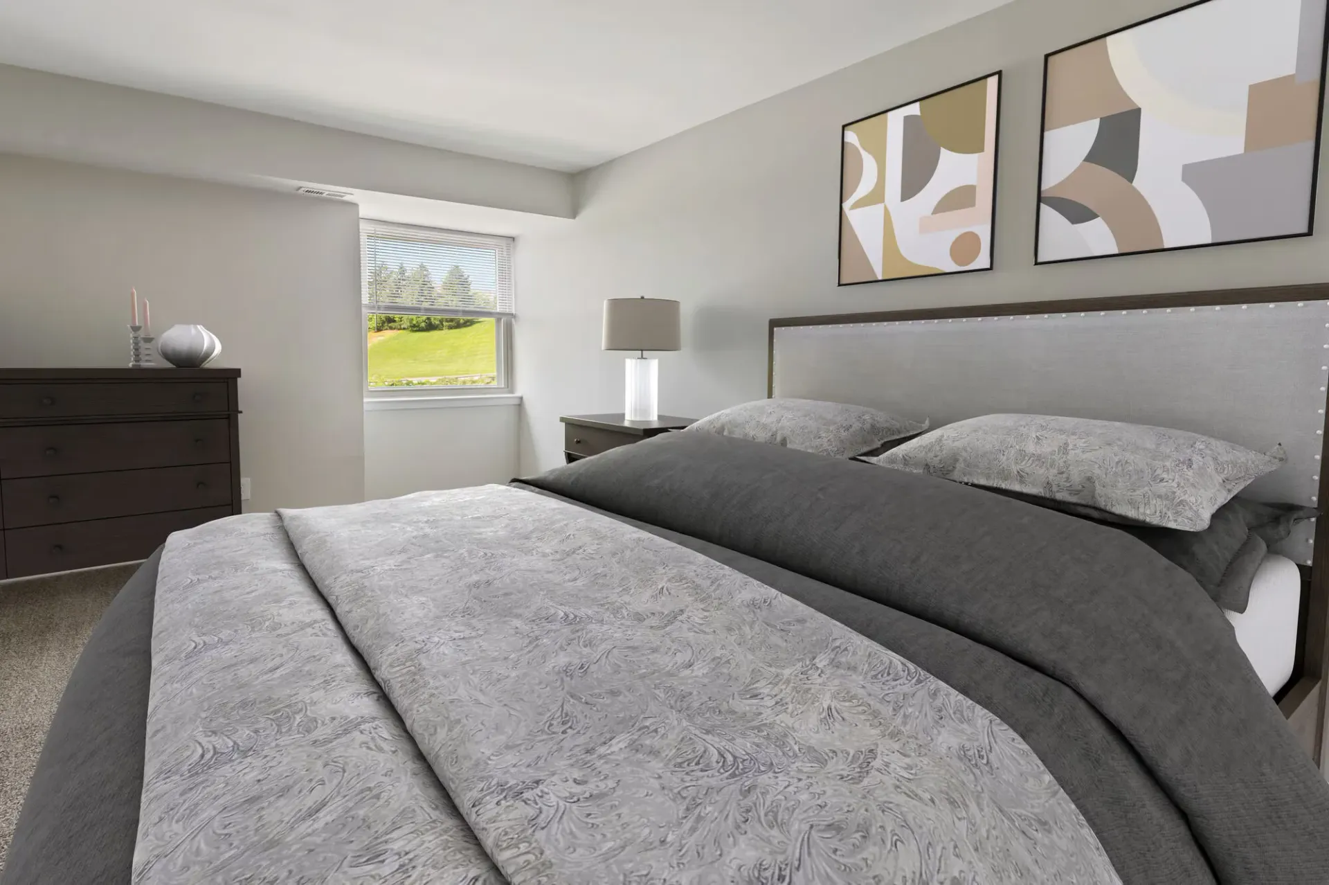 Bedroom in an apartment with a large bed, nightstand, dresser, and abstract wall art.