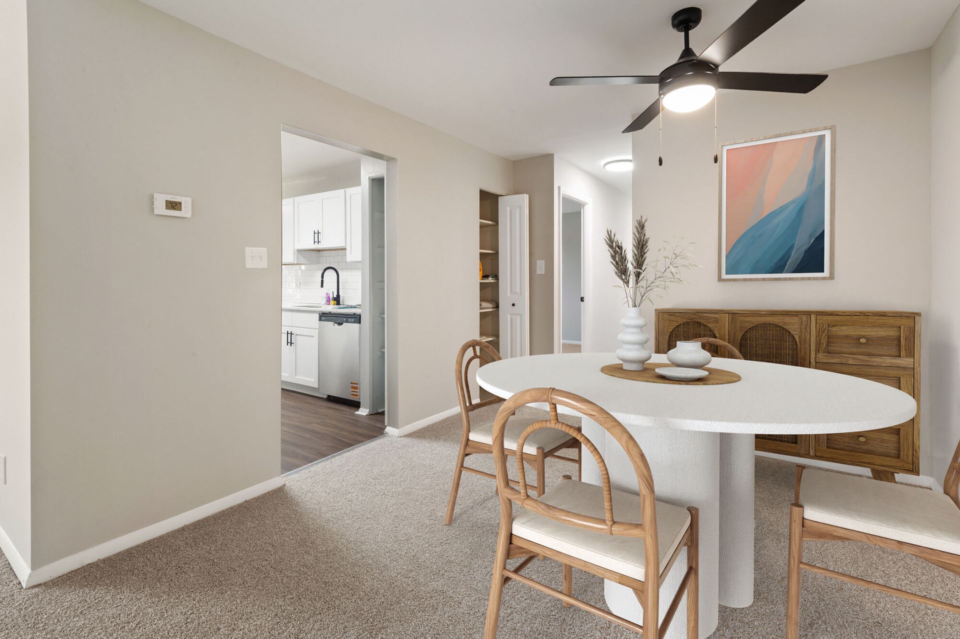 Dining area in an apartment with a round table, chairs, a sideboard, and a ceiling fan.