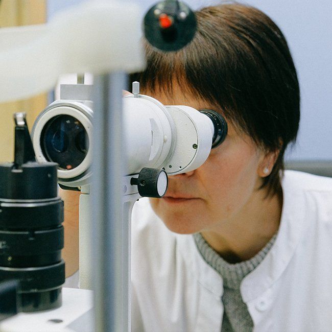 A woman in a white coat is looking through a microscope