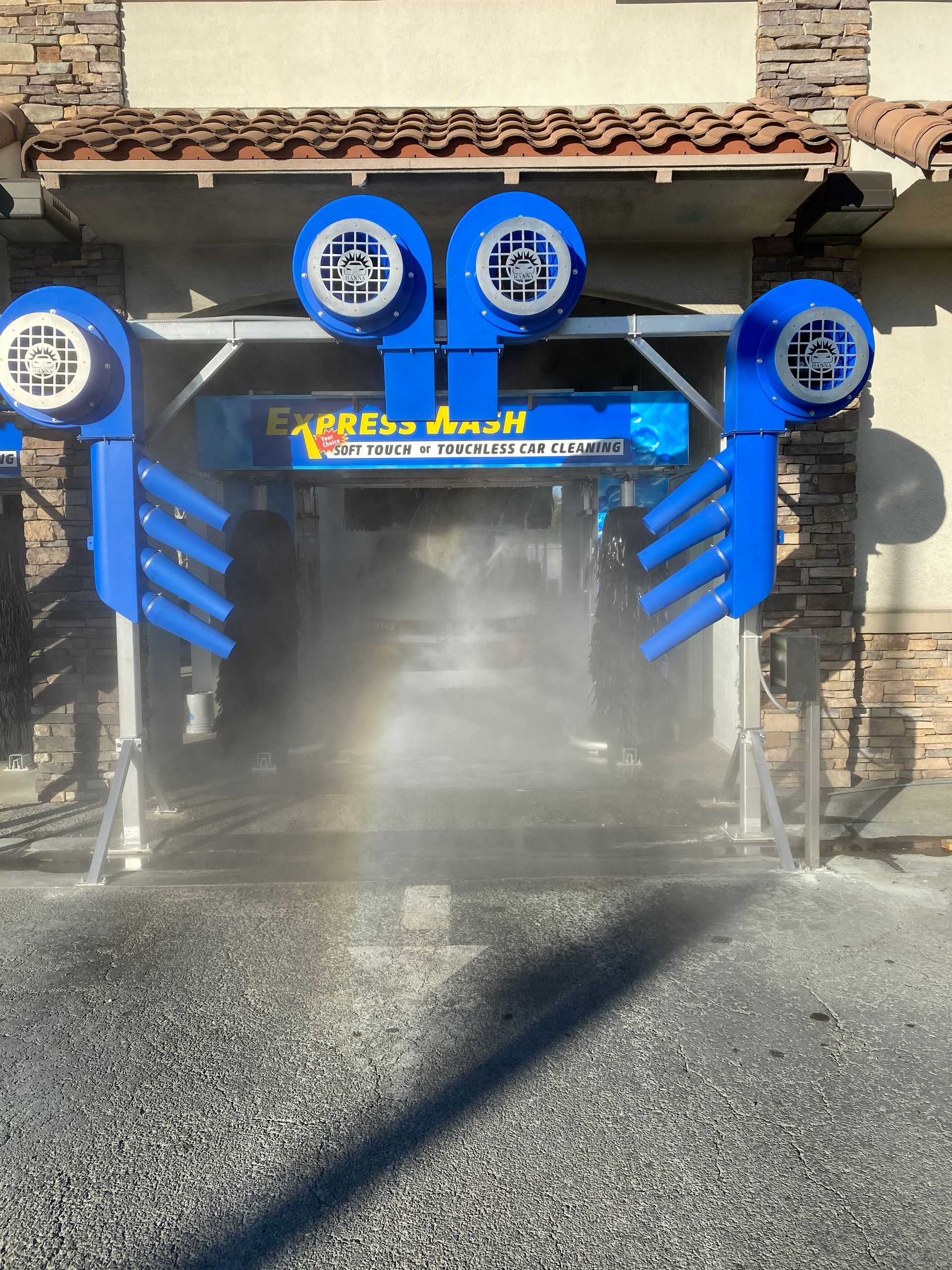 Blue car wash machine spraying water on a vehicle under a stone building awning