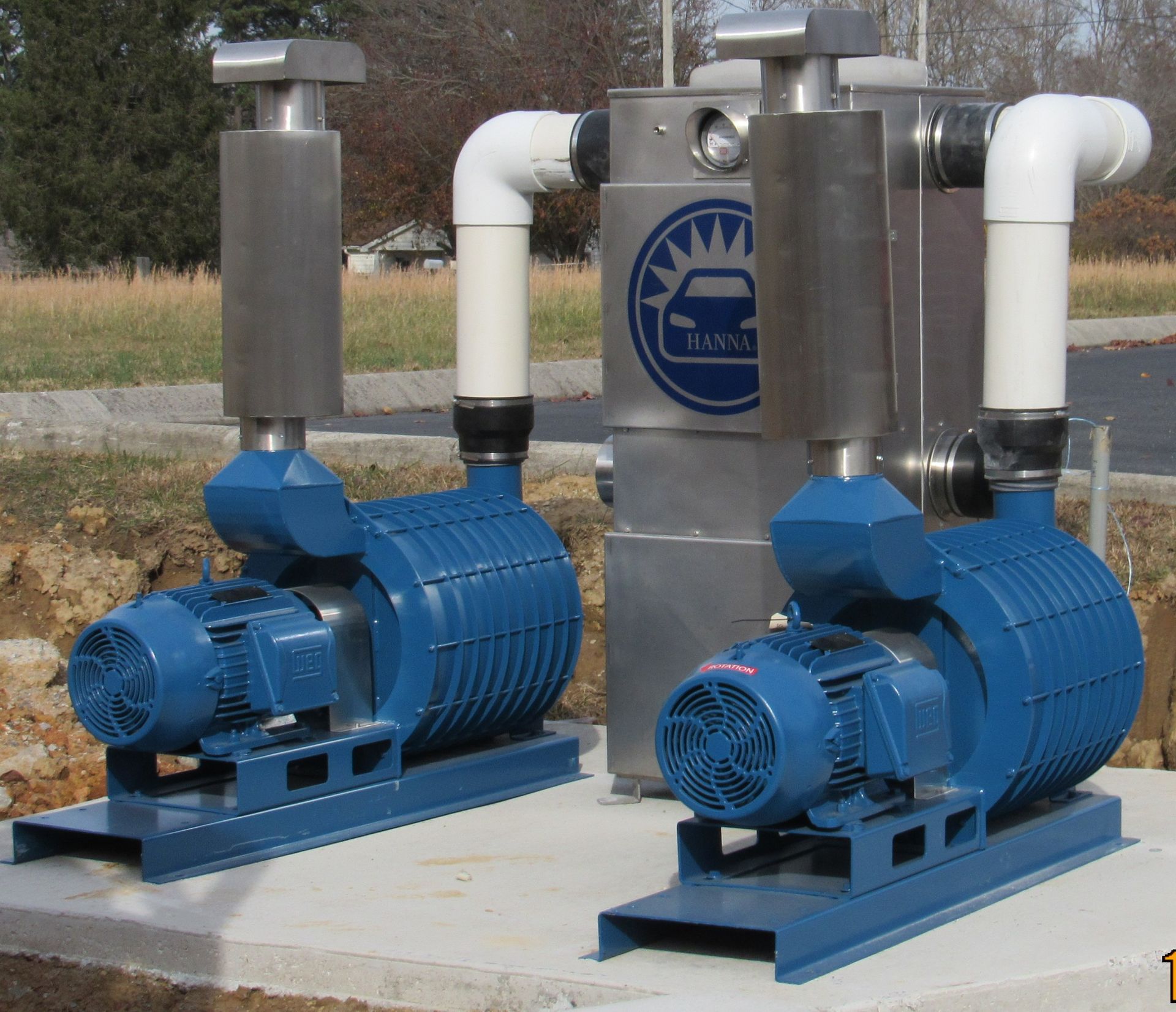 Two blue industrial pumps with metal piping on a concrete pad outdoors