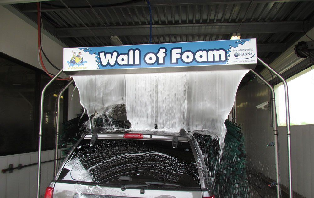 A car is being washed under a sign that says wall of foam