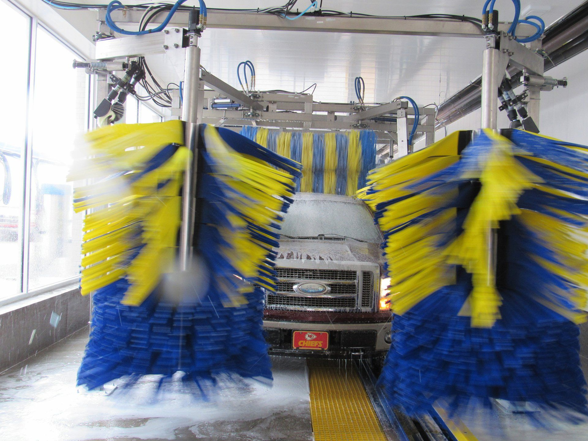 A truck is going through a car wash with yellow and blue brushes