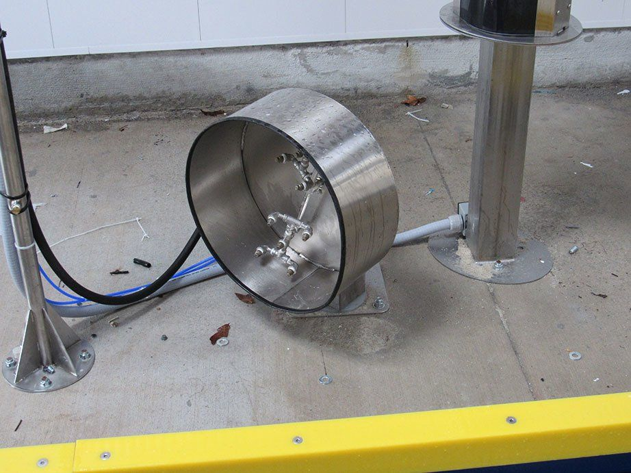 A stainless steel object is laying on the ground next to a yellow barrier.