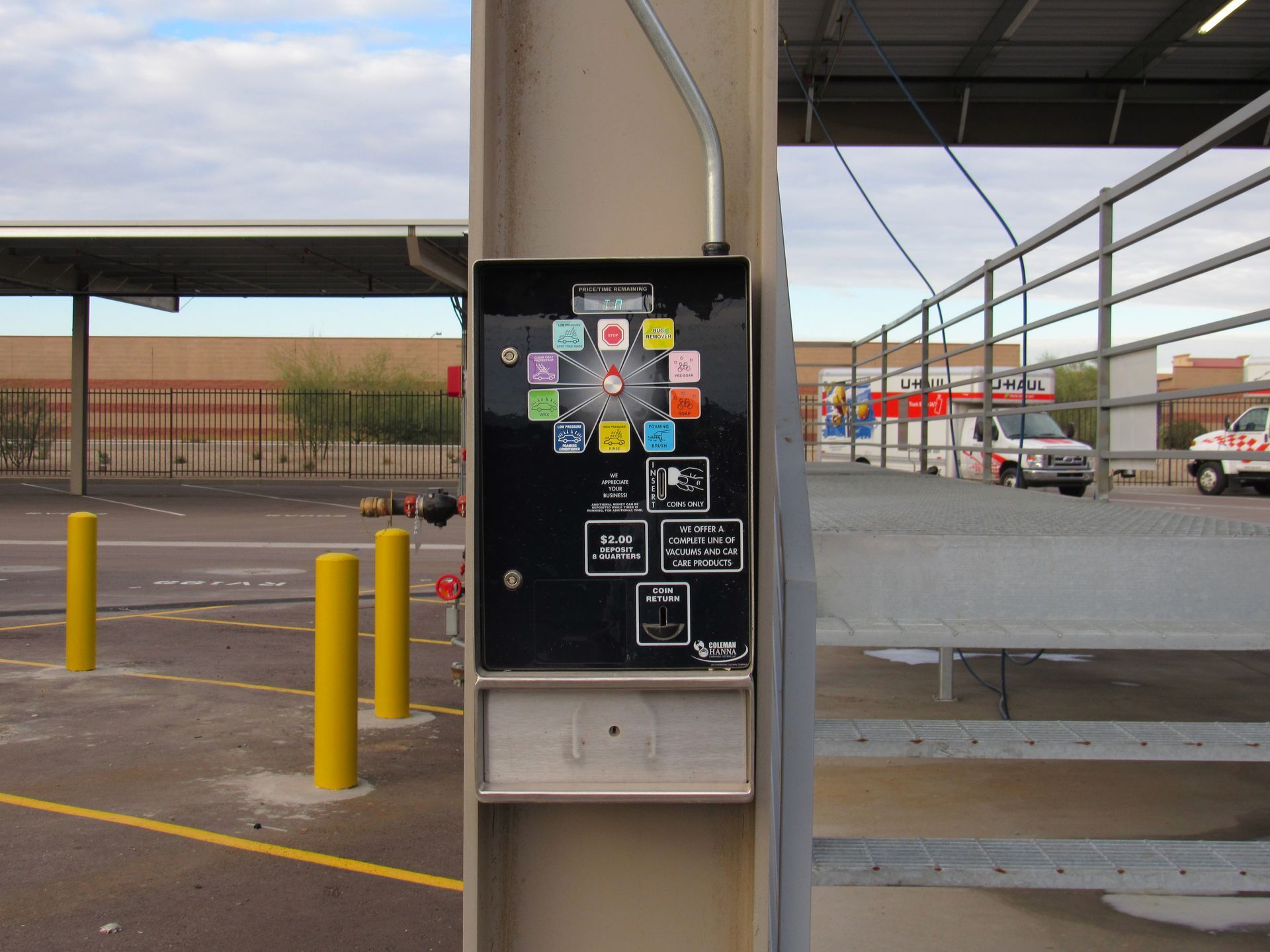 A black control panel with various buttons and labels mounted on a metal post near a gated area.
