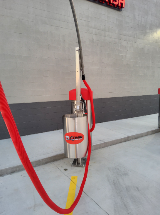 Red fire extinguisher on a wall-mounted stand with a hose and red safety cord in a parking area