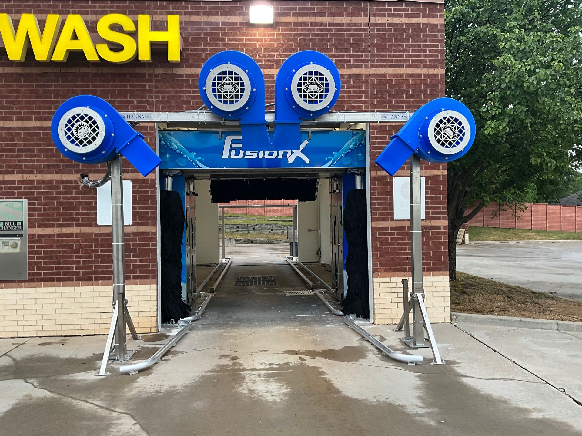 Car wash entrance with blue rollers and wet concrete outside a brick building.