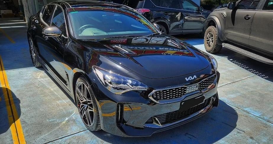Black Kia Stinger car parked outside, reflecting sunlight.