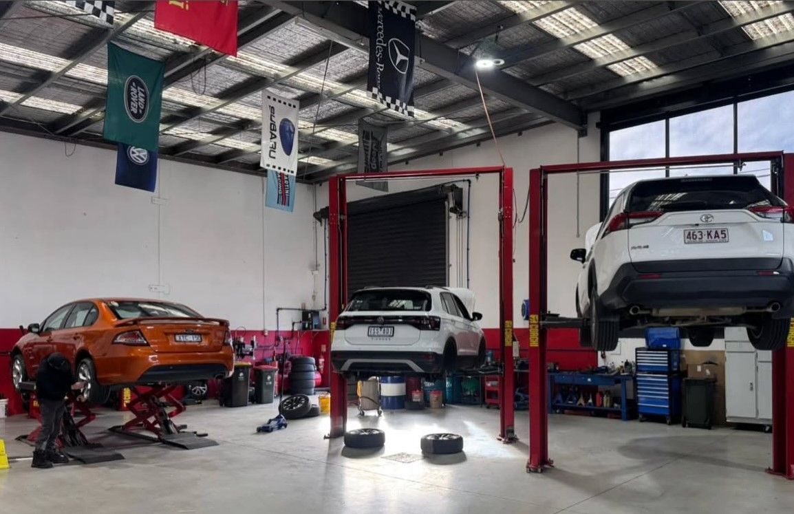 Cars on lifts in an auto repair shop. Red lifts, banners overhead, orange and white vehicles.