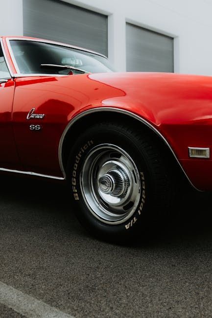 Red vintage Chevrolet Camaro, partially shown, parked. Black tires, chrome hubcaps.