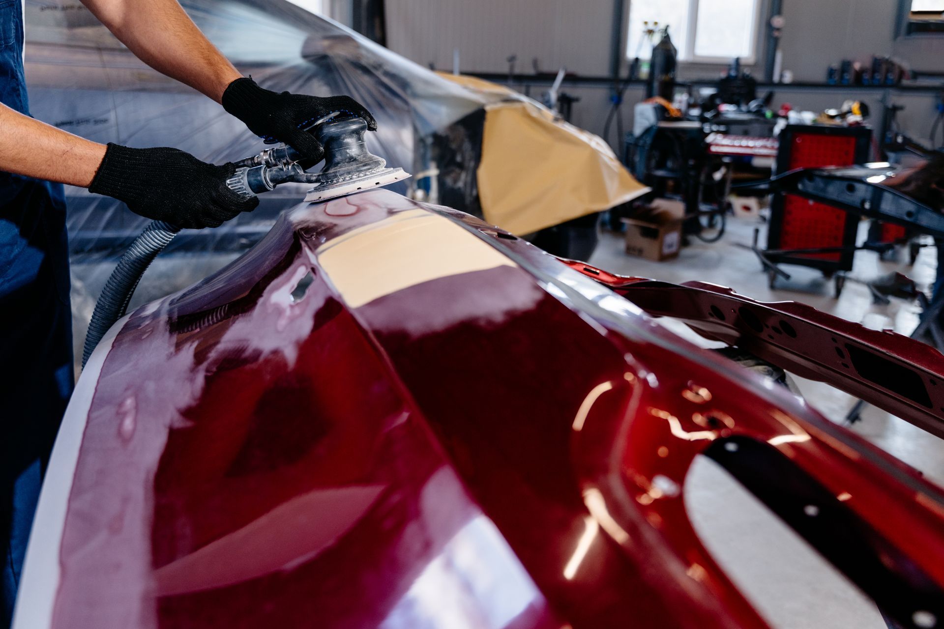 A person sanding a car bumper in a body shop, preparing for paint.