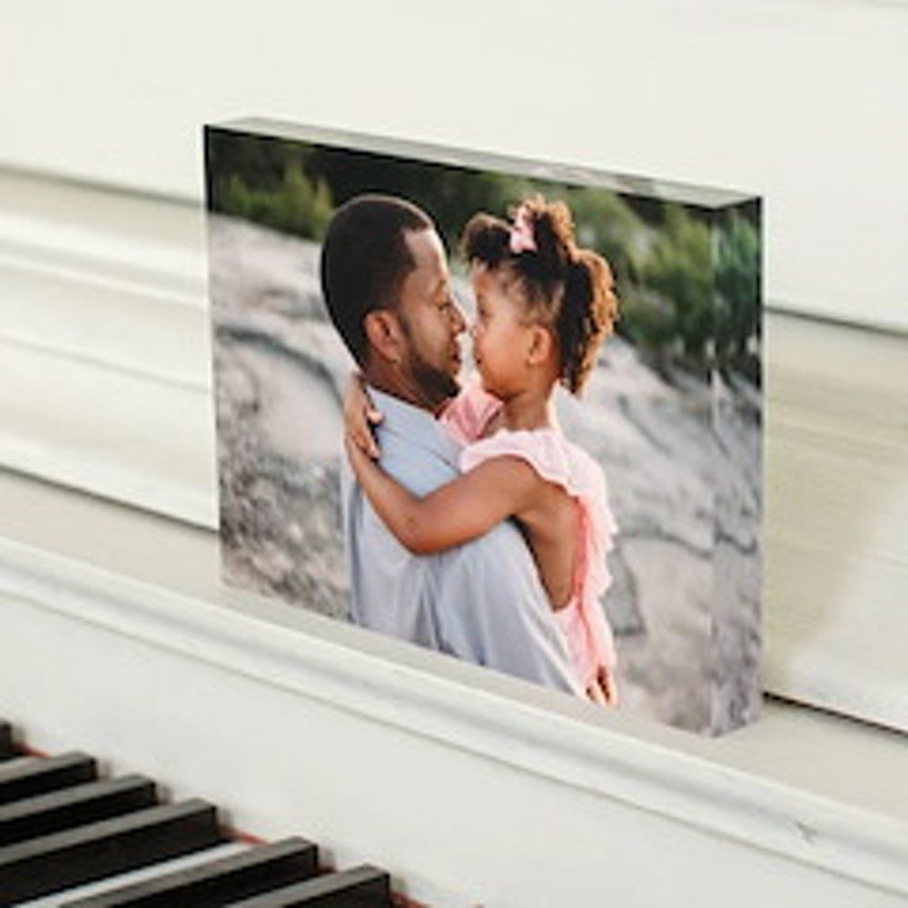 Un bloc photo représente un homme tenant un jeune enfant. Ils se font face, souriants. Posé sur un piano.