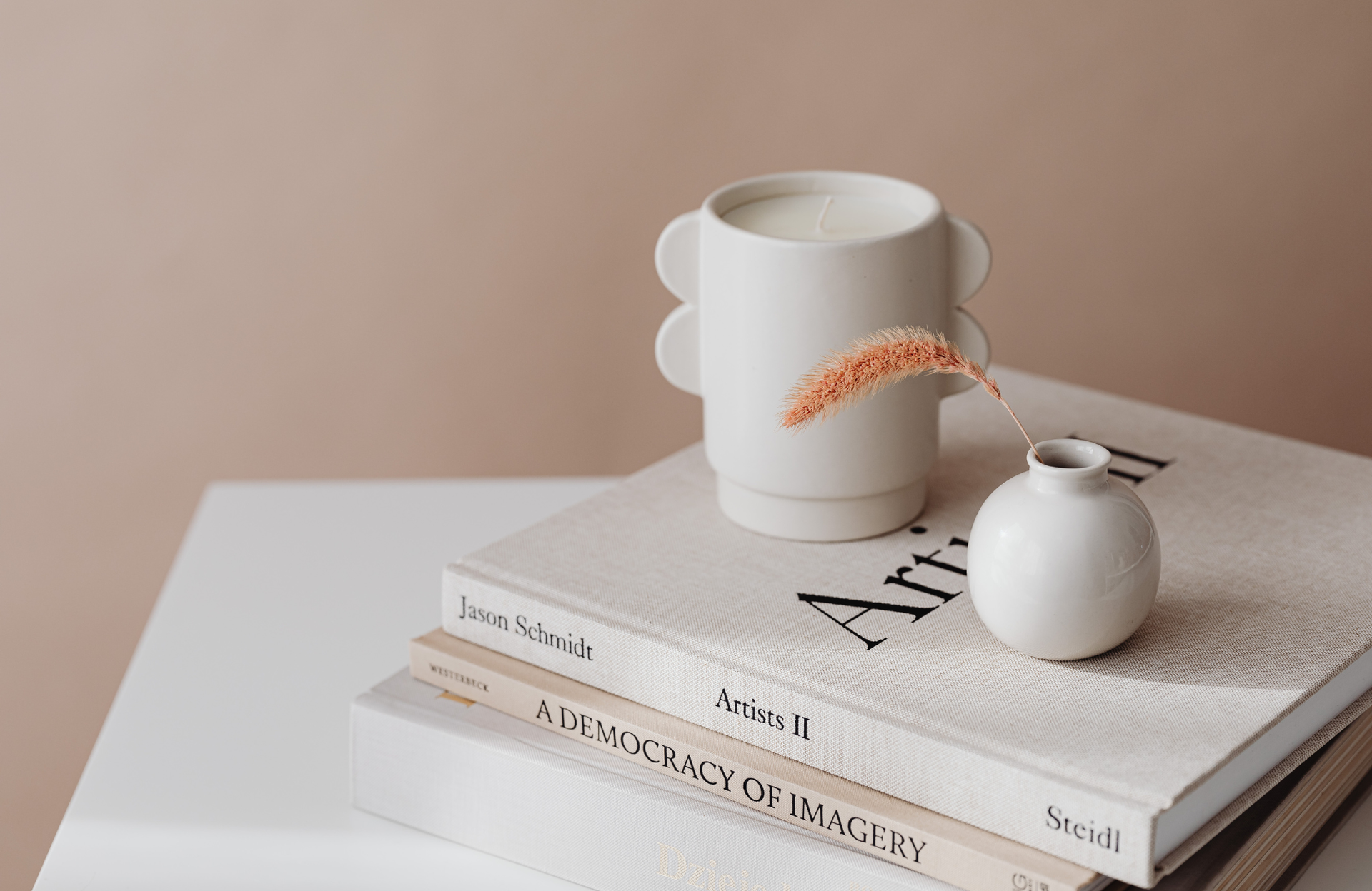 Minimal beige still life with stacked books, a white mug, and a small white vase on a table