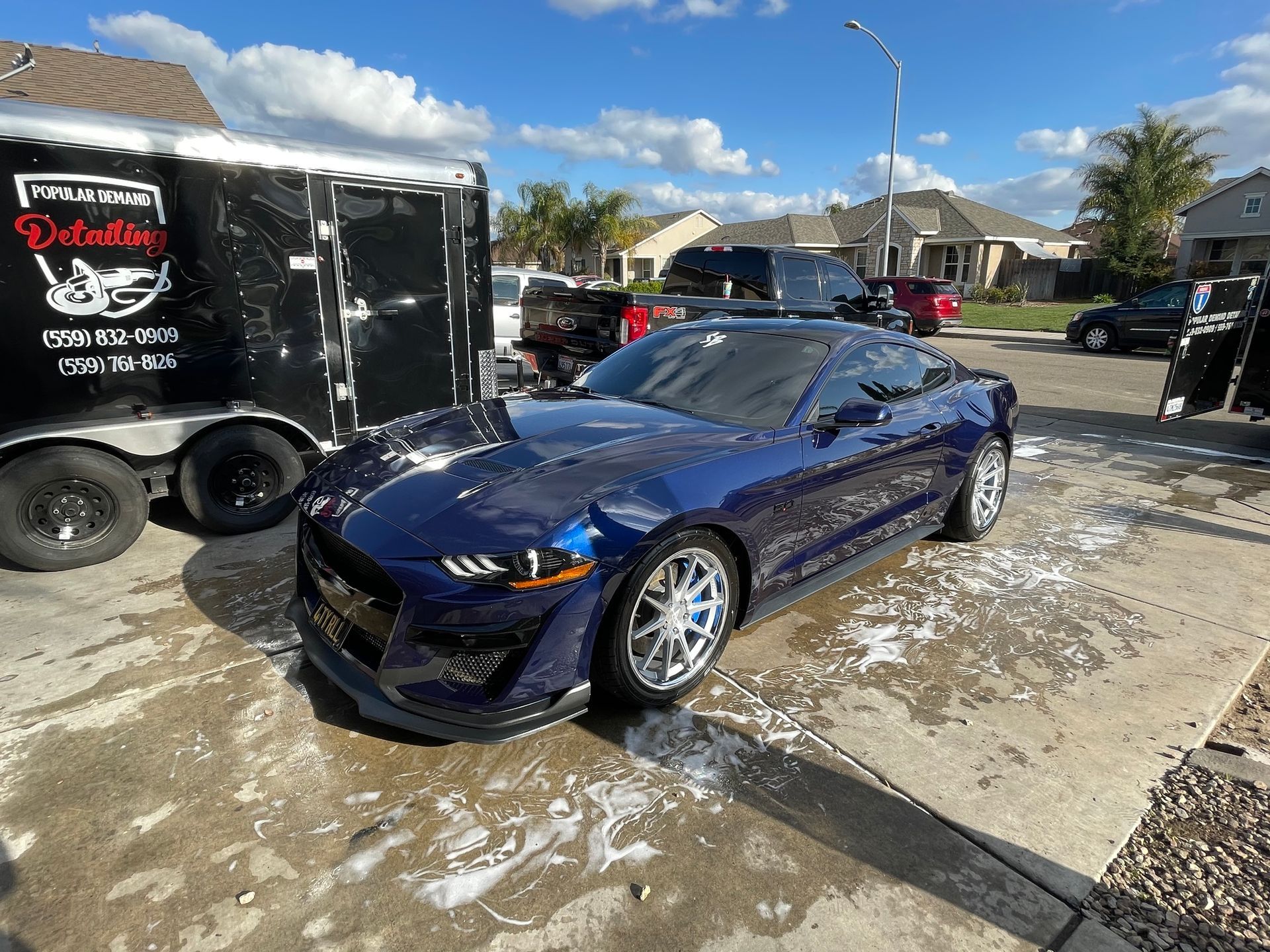 A blue mustang is parked in a parking lot next to a trailer.