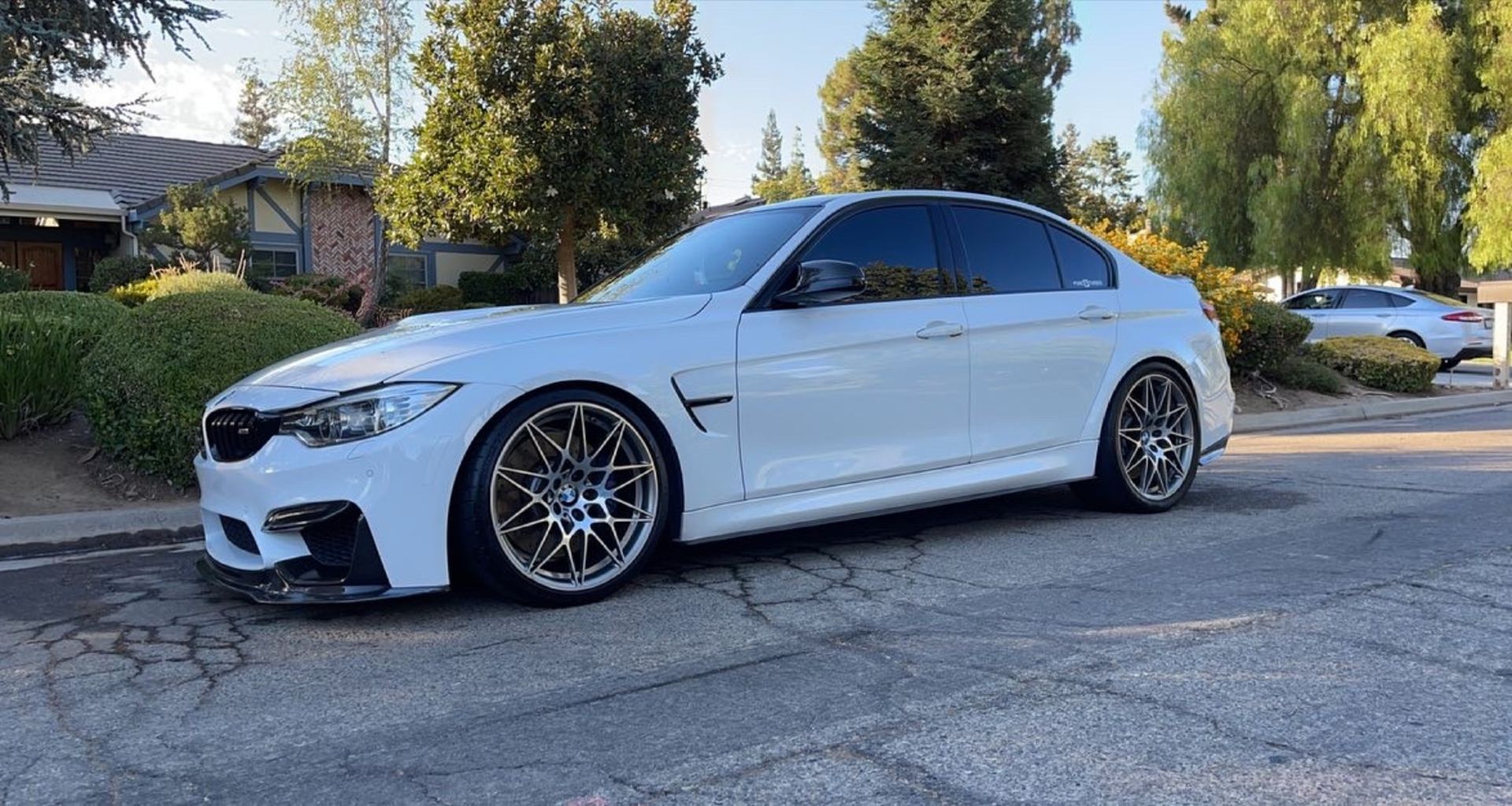 A white bmw m3 is parked on the side of the road.