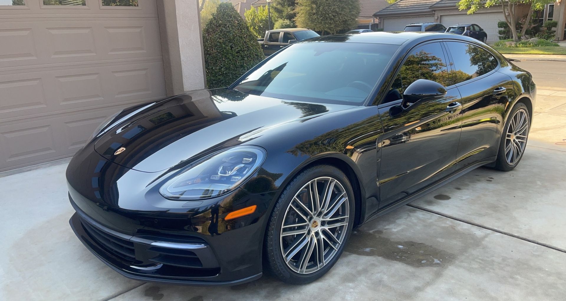 A black porsche panamera is parked in a driveway next to a garage.