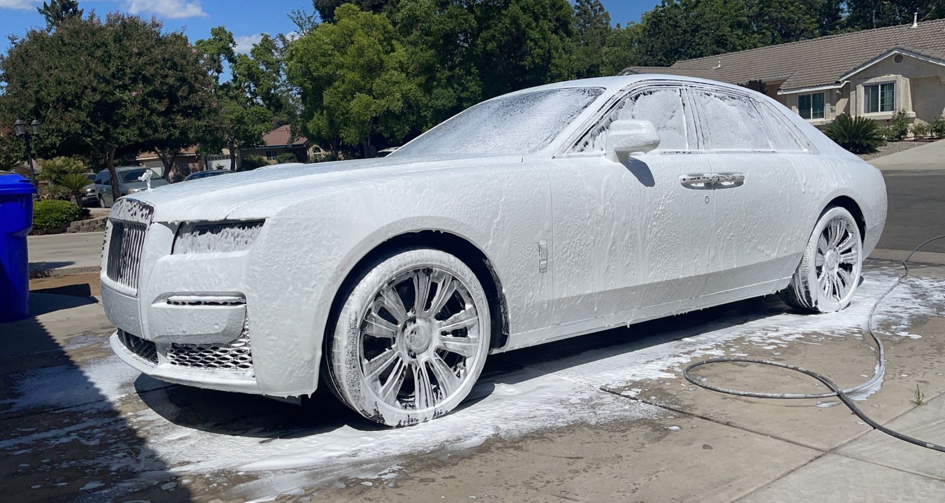 A white car covered in foam is parked on the side of the road.