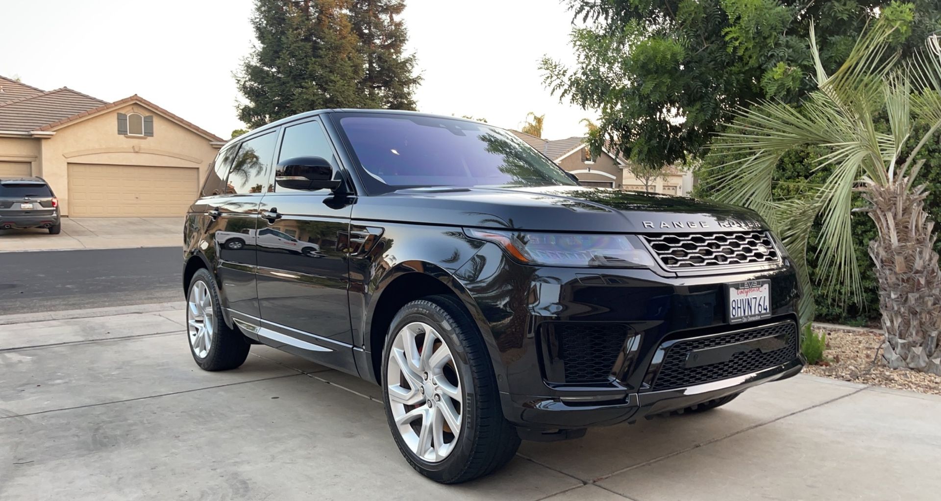 A black range rover sport is parked in a driveway next to a palm tree.