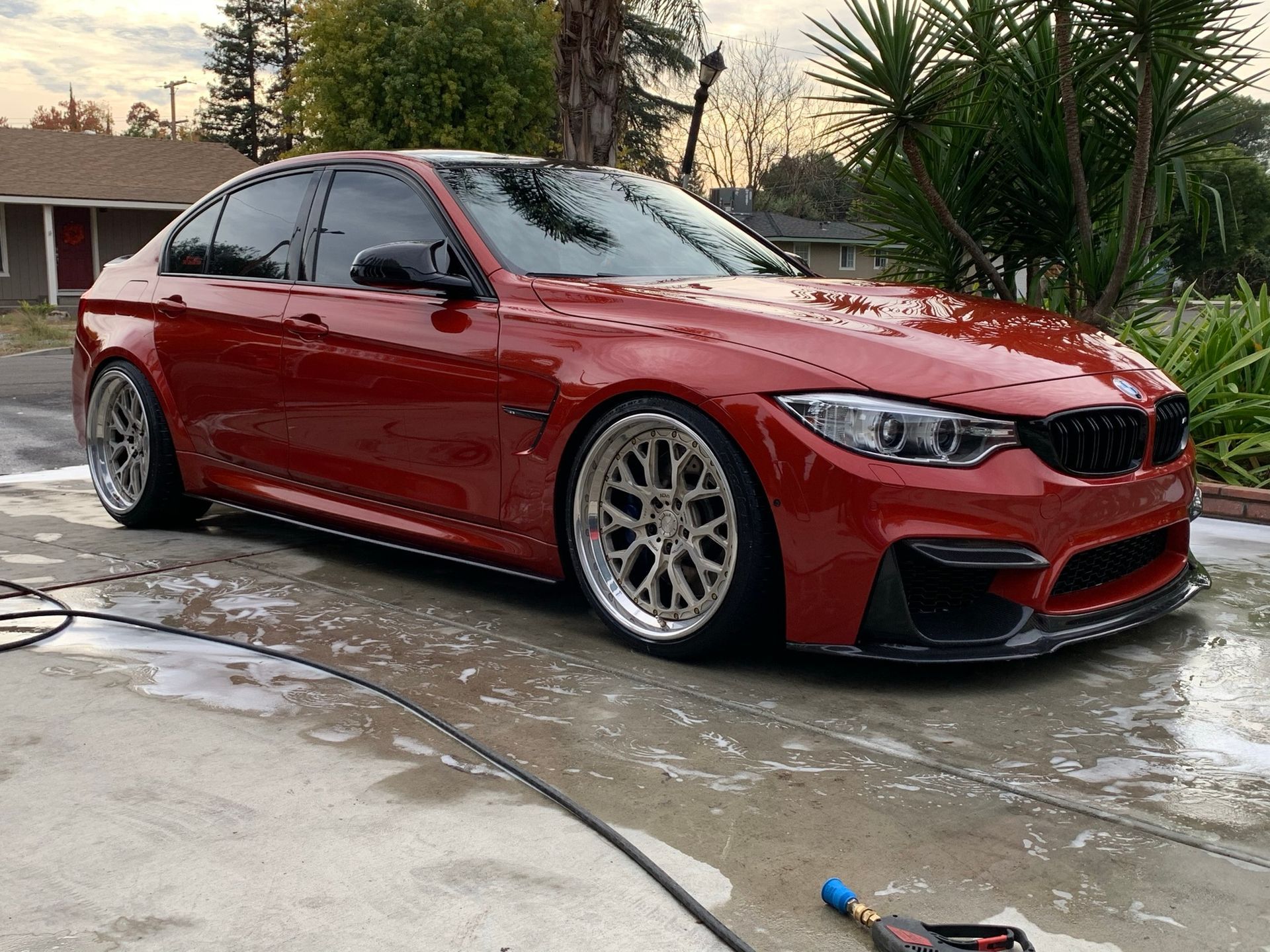 A red bmw m3 is parked in a driveway next to a hose.