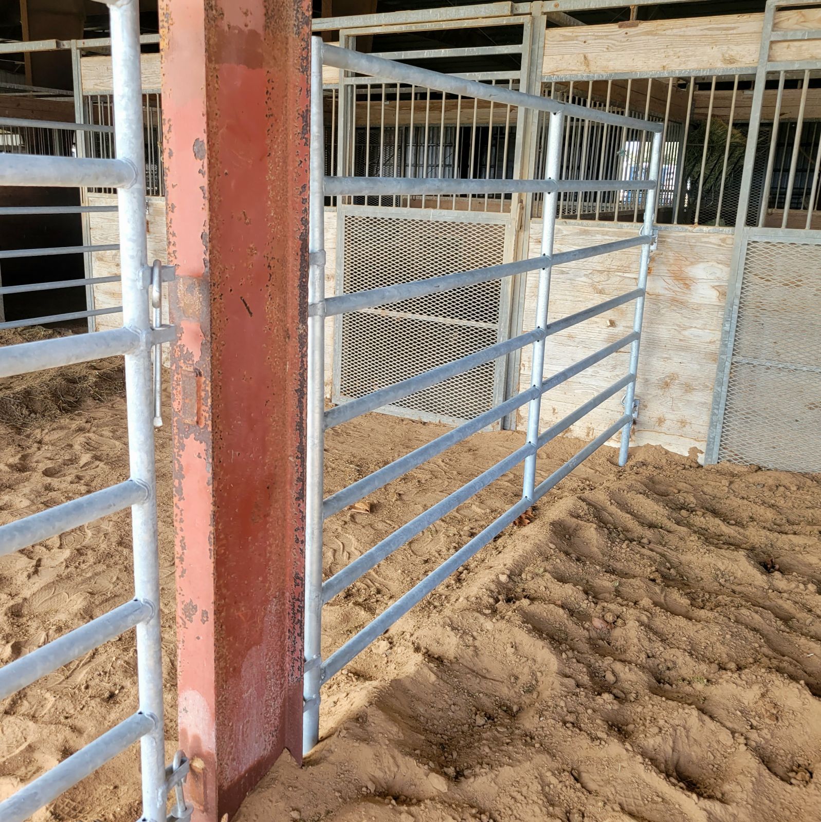 A metal fence surrounds a dirt area in a barn