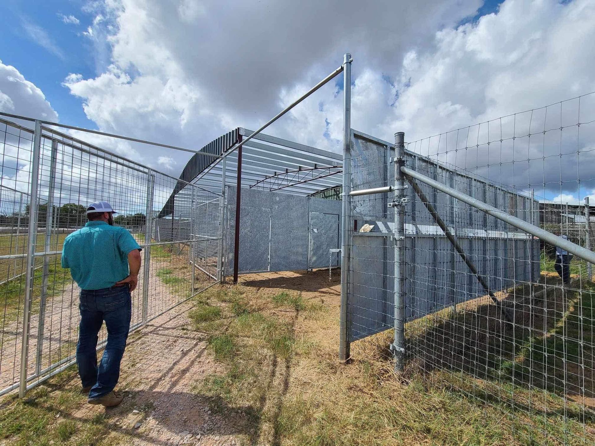 A man is standing in front of a fence in a field.