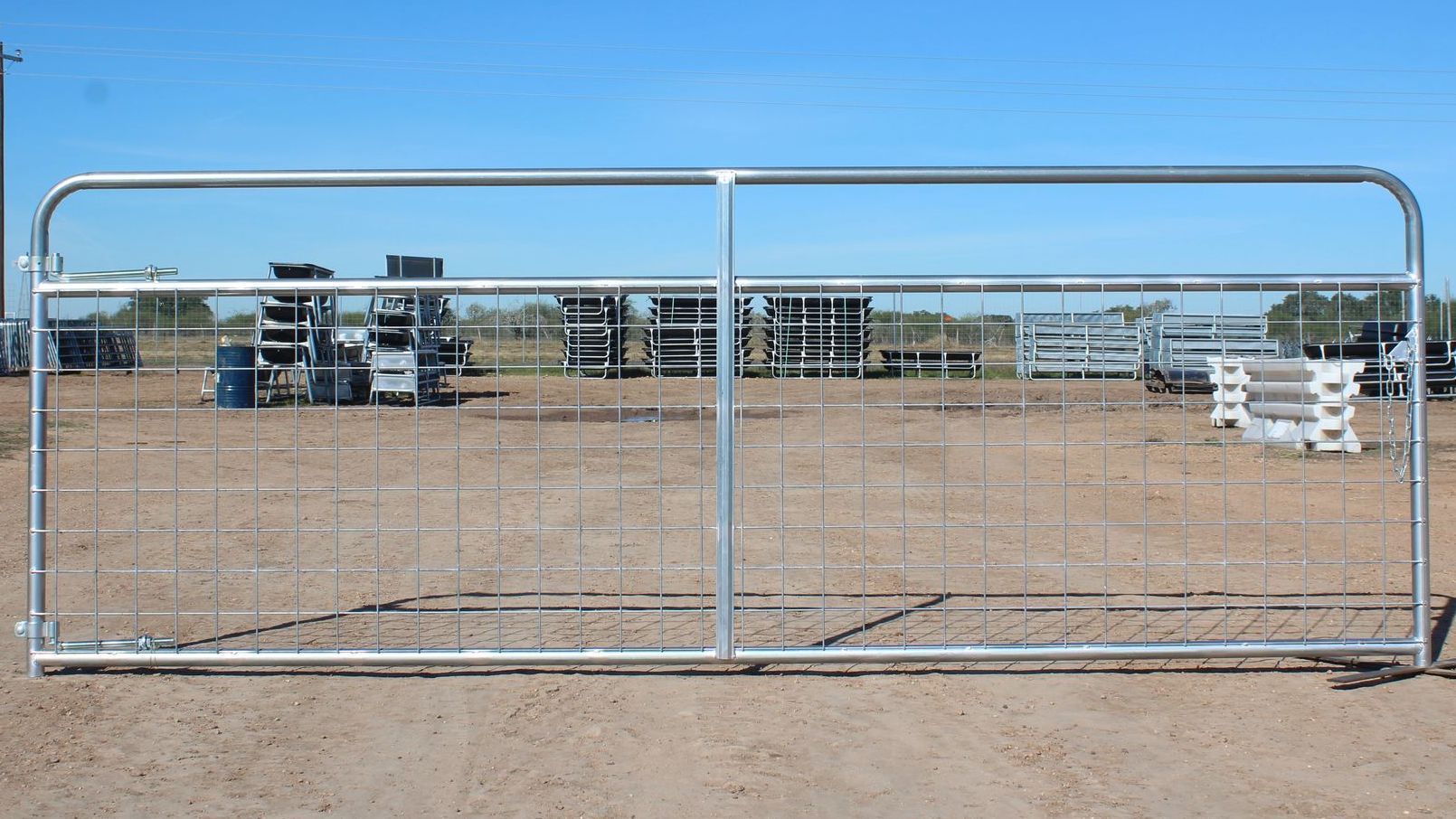 A galvanized gate is sitting in the middle of a dirt field.