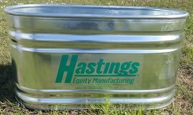 A metal tub with the word hastings on it is sitting in the grass.