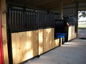 A horse stable with wooden walls and black fences.