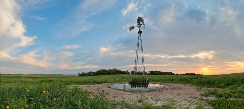 A windmill is sitting in the middle of a field at sunset.