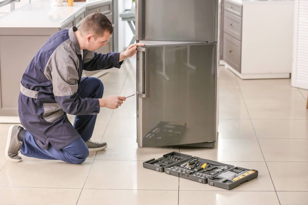 A Man Is Fixing a Refrigerator in A Kitchen — Care Mechanical Services in Wagga Wagga, NSW