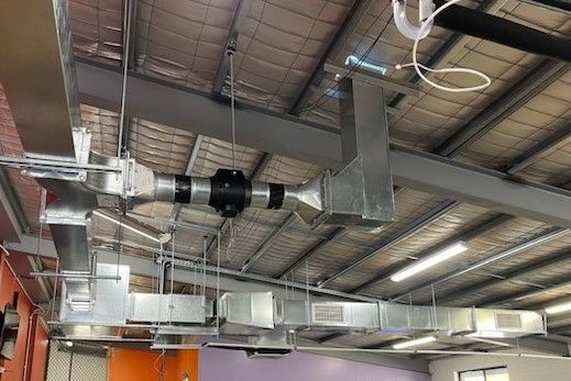 Industrial ceiling with metal ductwork, vents, and exposed beams in a warehouse-like interior. - Care Mechanical Services in Wagga Wagga, NSW