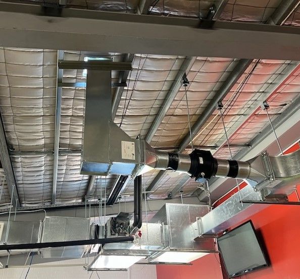 Industrial ceiling with exposed ductwork, metal beams, and a red wall in an unfinished interior space - Care Mechanical Services in Wagga Wagga, NSW
