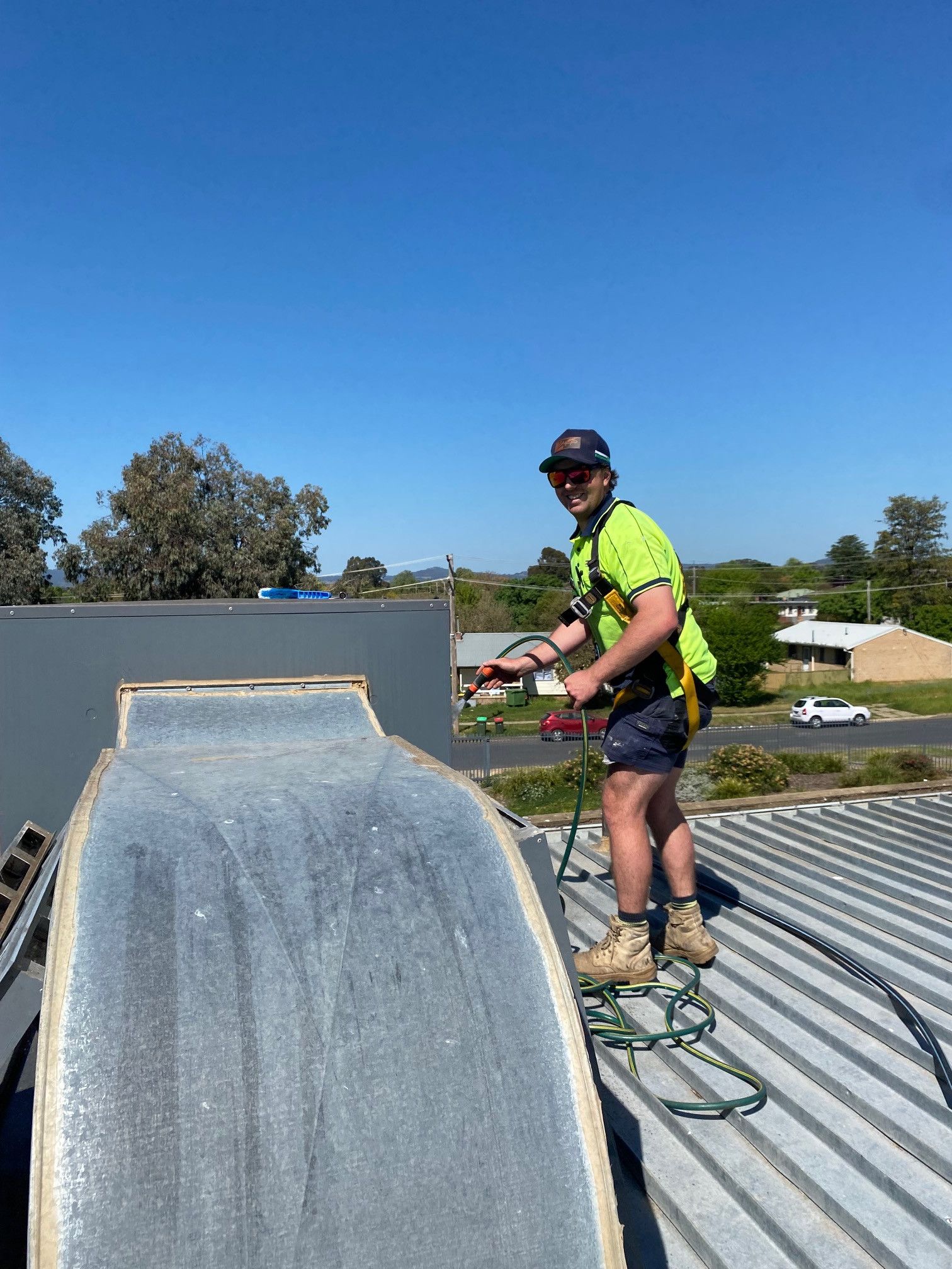 Worker in neon shirt standing on a roof beside a large metal vent under a clear blue sky - Care Mechanical Services in Wagga Wagga, NSW