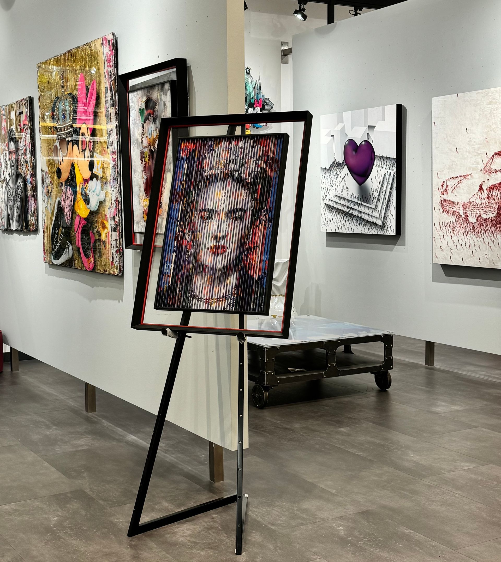 Art gallery with paintings on walls, including a framed piece on a stand.