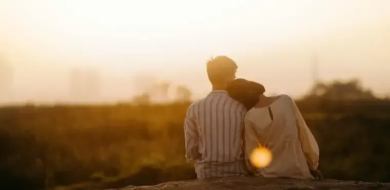 A couple sitting together in a field at sunset
