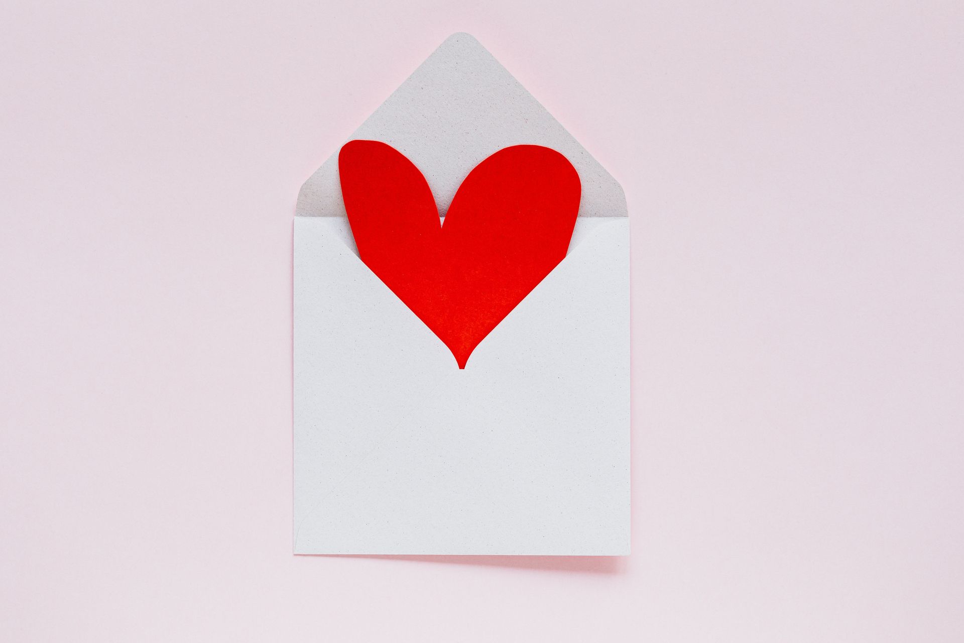 White envelope with a red heart peeking out from the top on a pale background