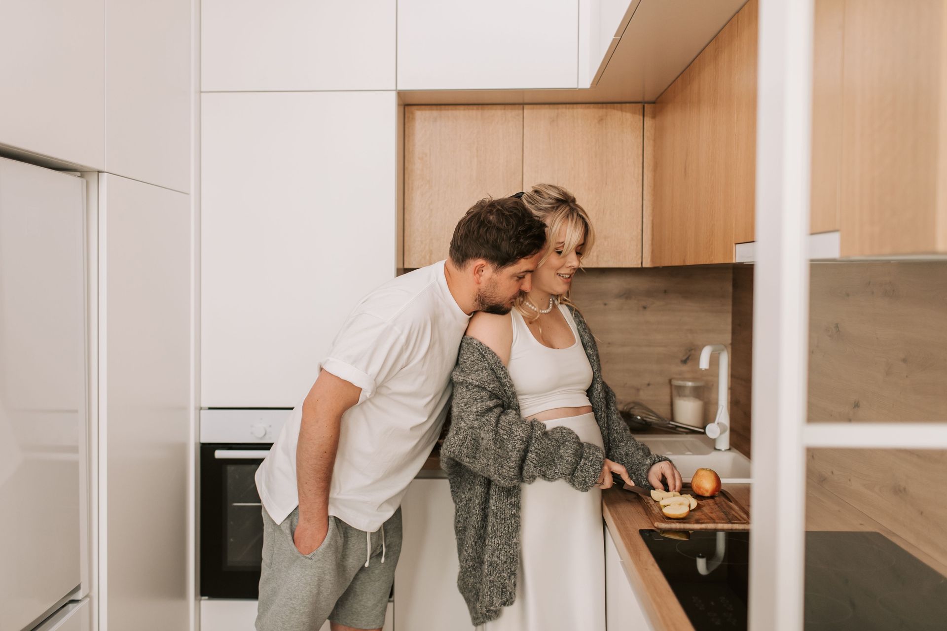 Two people preparing food together in a modern kitchen, leaning over a countertop with fruit and a cutting board.
