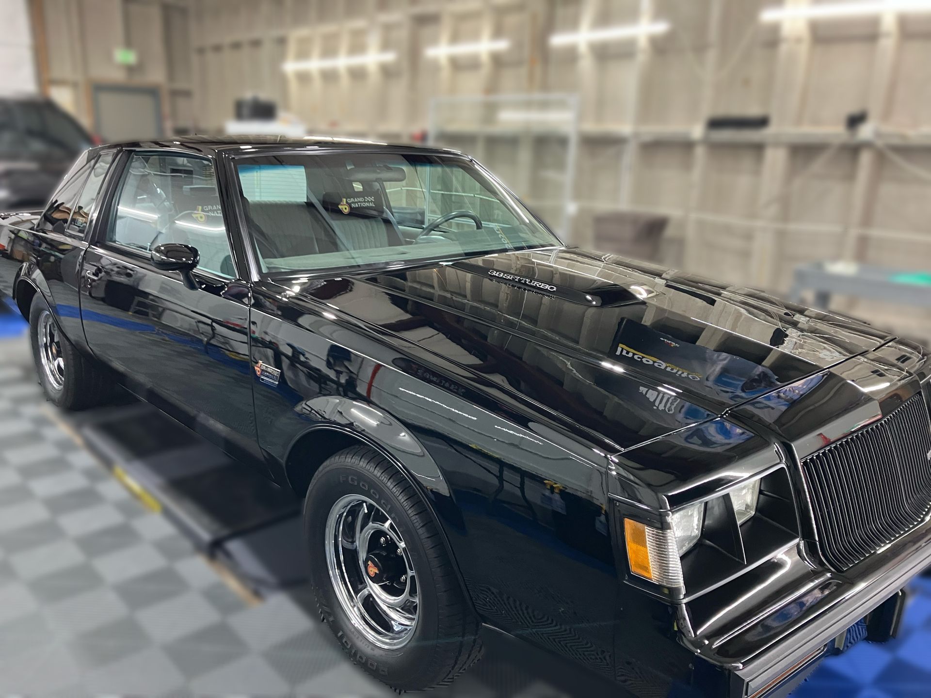 Black classic muscle car with chrome details parked indoors on a checkered floor