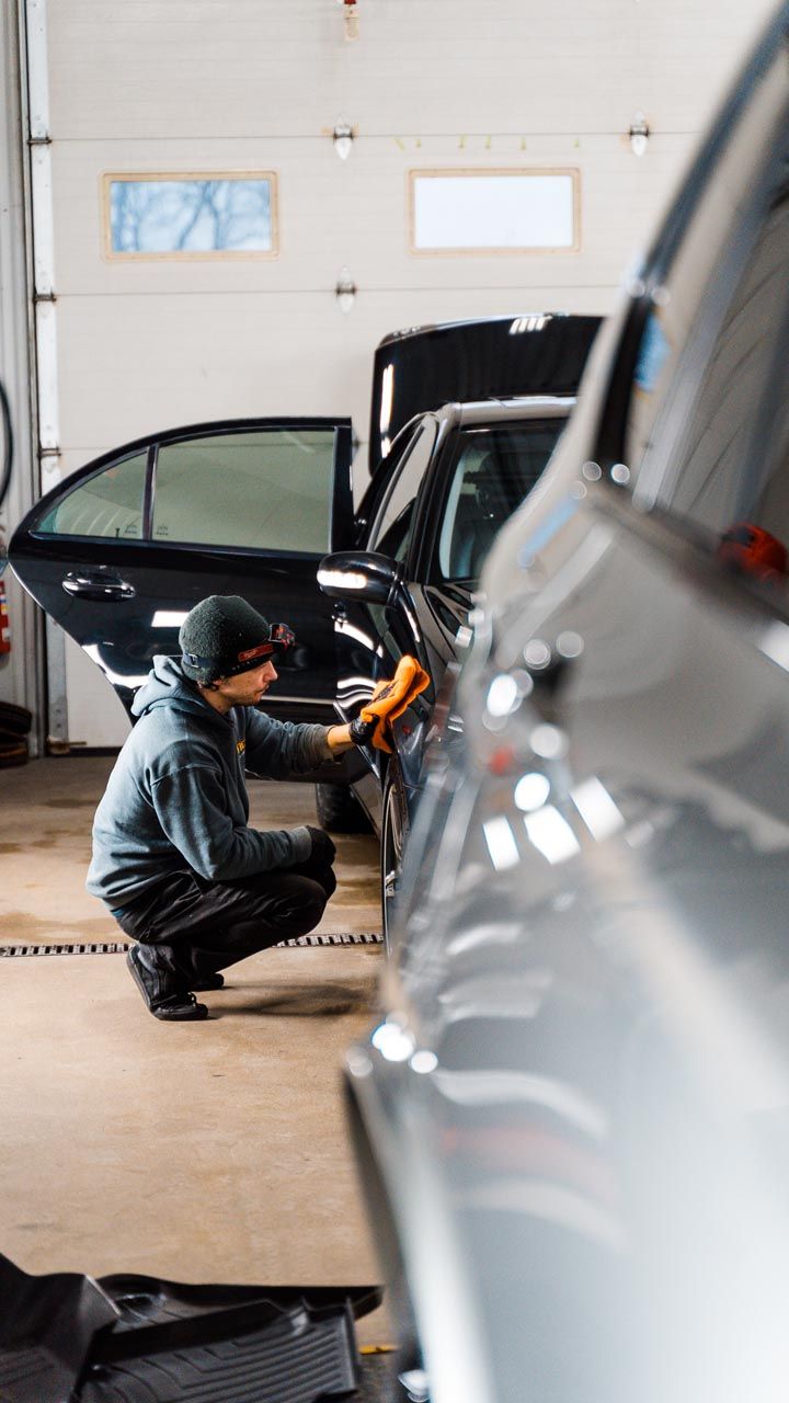 A man is kneeling down to clean a car in a garage.