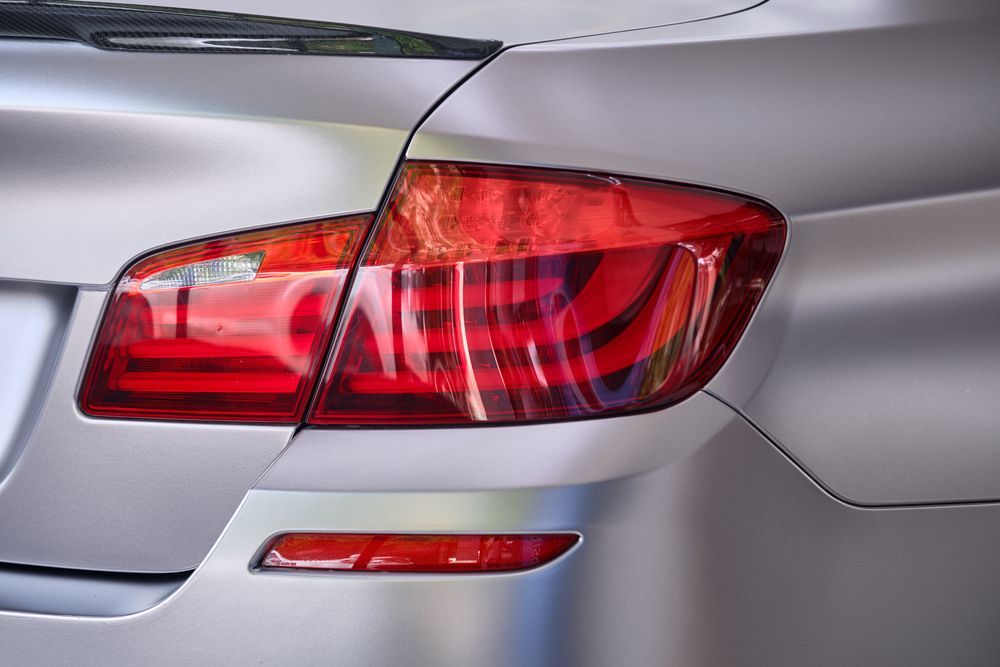 Close-up of a silver car's rear taillight assembly and bumper against a matte finish body.