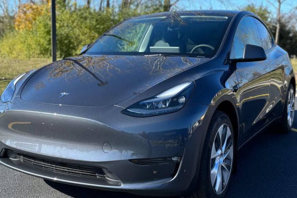 A sleek, gray Tesla parked outdoors on a sunny day, with reflections of trees on its glossy surface, emphasizing the importance of UV protection for vehicle paint.
